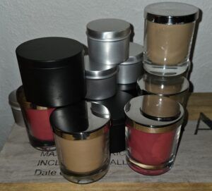 Handmade soy candles in black and silver tins and glass jars arranged on a wooden surface, showcasing a small batch of Nordic-inspired scented candles by FjordLume.